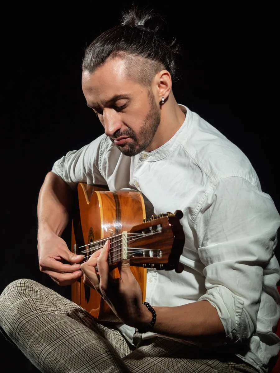 Gitarzysta flamenco grający na gitarze klasycznej, oświetlony na czarnym tle (zdjęcie poglądowe, nie przedstawia własnej obsady Corral de la Morería)